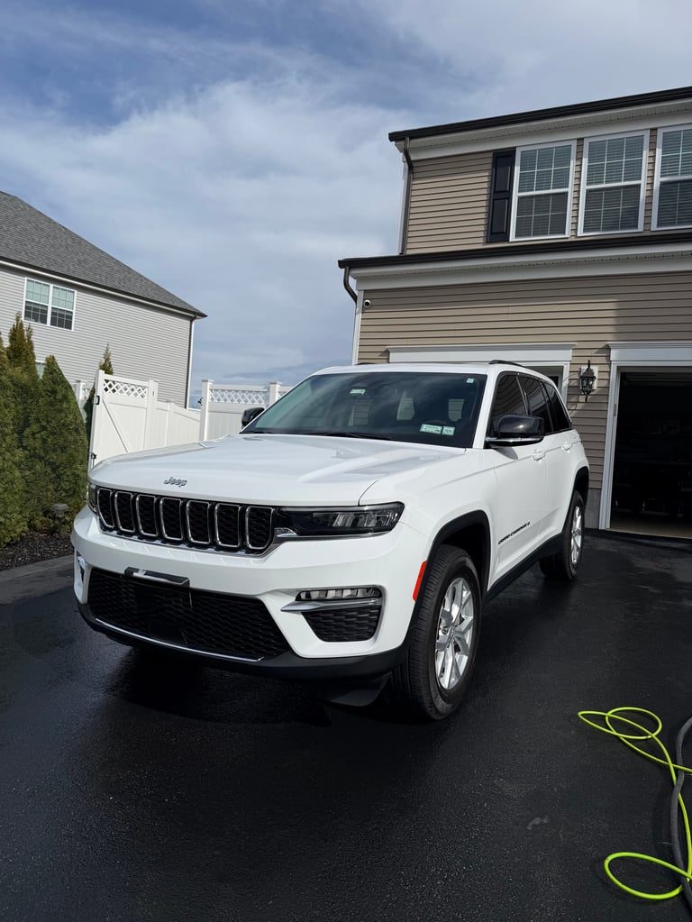 White Jeep Grand Cherokee parked in a residential driveway with houses and cloudy sky in the background