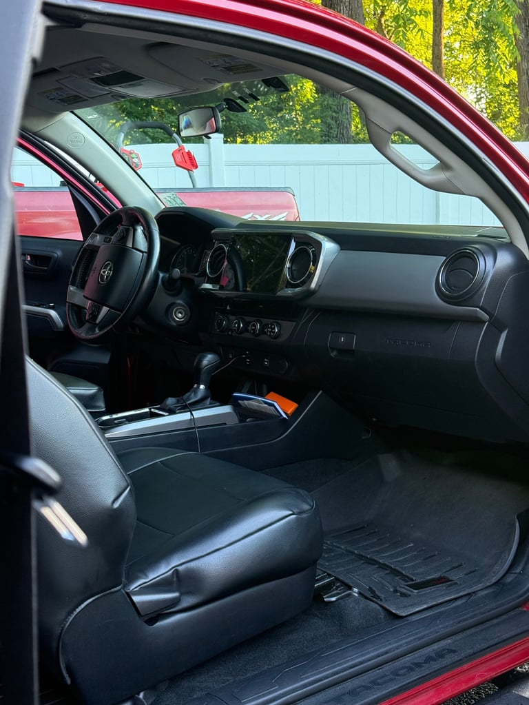Interior view of red pickup truck with open driver door, showing black leather seats, steering wheel, and dashboard